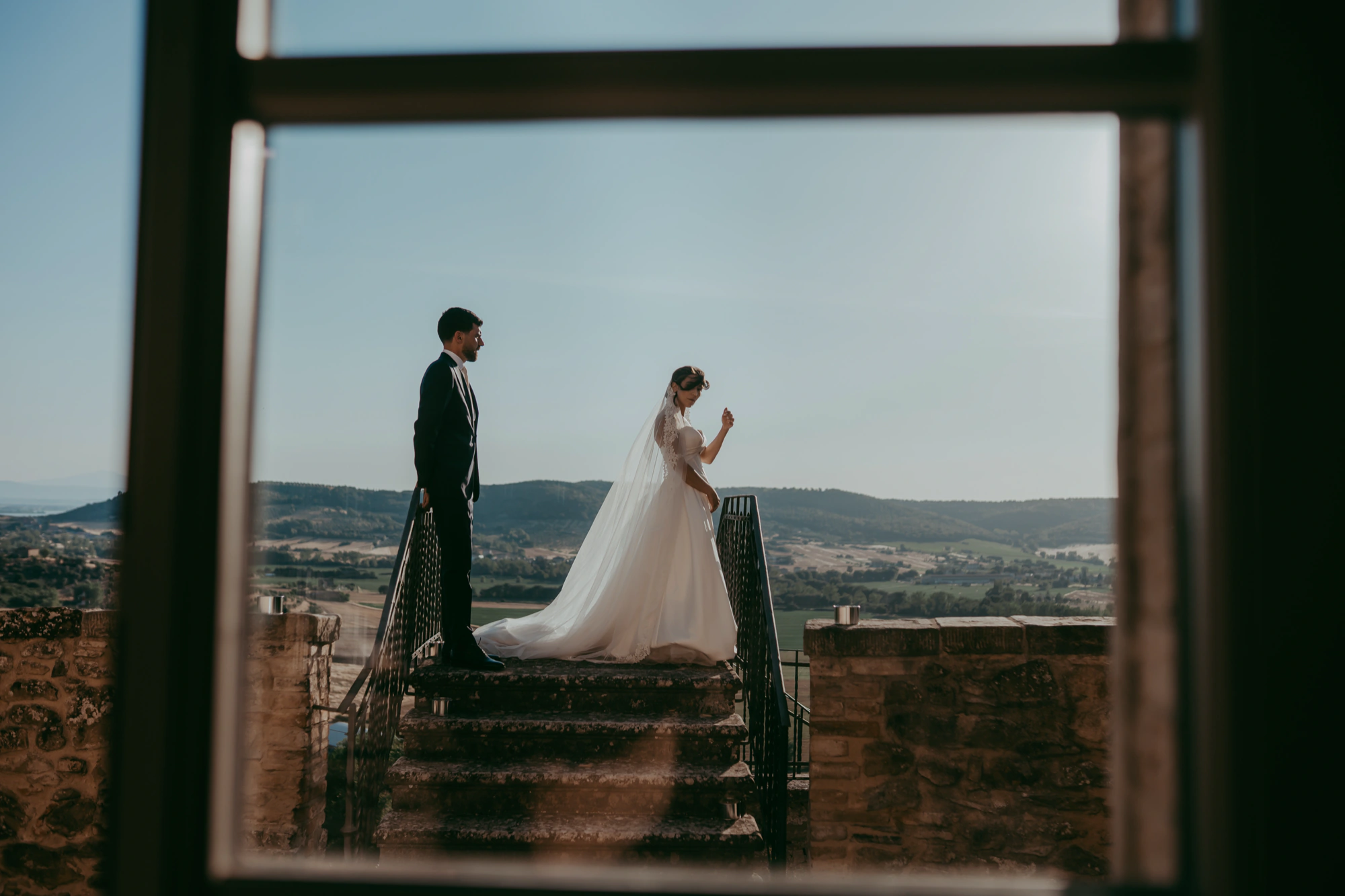 Sposi su una terrazza di pietra visti attraverso una finestra, con le colline sullo sfondo — fotografia di Andrea Mortini
